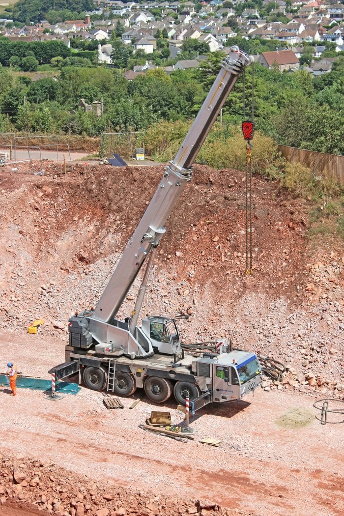All terrain crane with its telescopic boom extended, working in a quarry excavation site