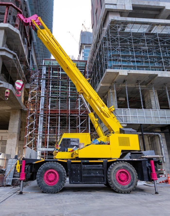 Yellow rough terrain crane on large off-road tires, lifting near scaffolding at a construction site